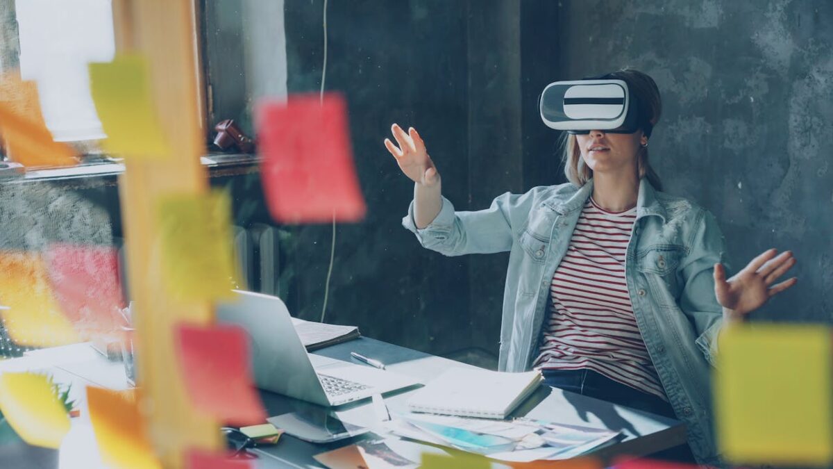 Woman in a creative workspace using a VR headset, surrounded by sticky notes and a laptop.
